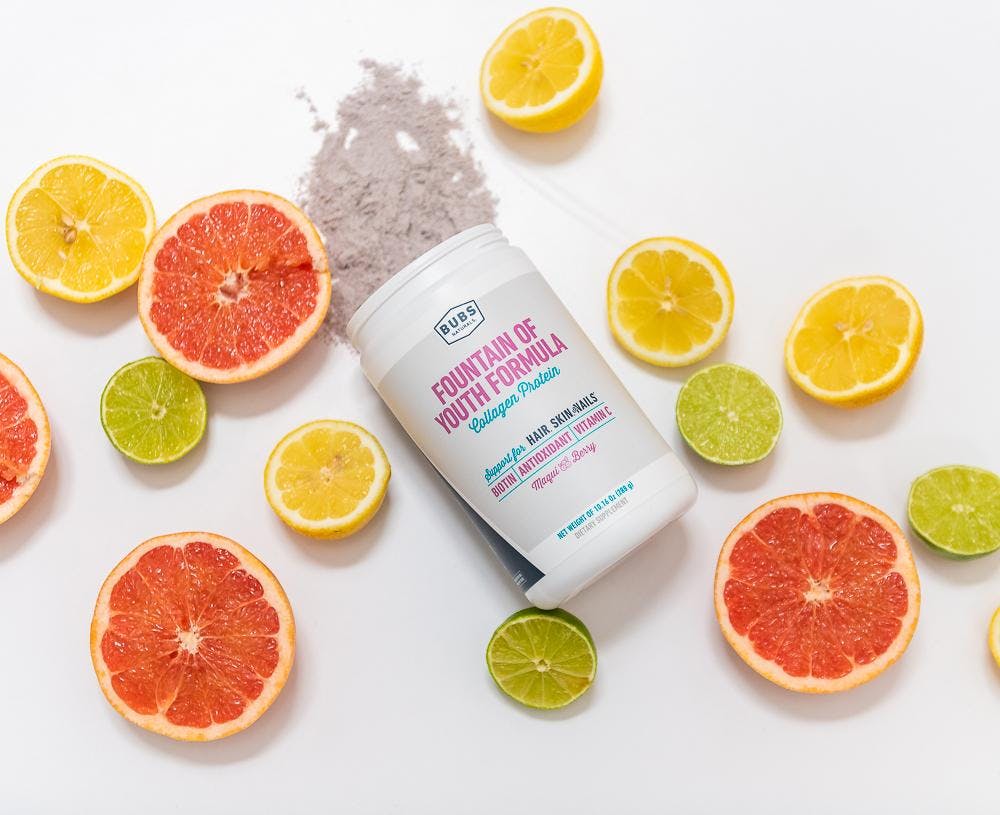 Fountain of Youth Formula Collagen Protein Powder container with powder overflowing surrounded by grapefruit, lemons and limes