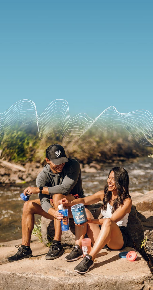 Happy couple adding Bubs collagen peptides powder to their drinks on a hike